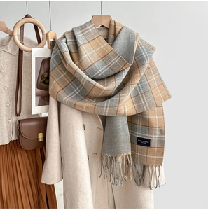 Détail d'une écharpe à carreaux beige et gris avec franges sur un manteau en laine