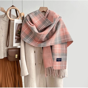 Détail d'une écharpe à carreaux rose et gris avec franges sur un manteau beige