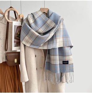 Détail d'une écharpe à carreaux bleu et beige avec franges et étiquette sur un manteau beige