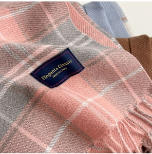 Gros plan sur la texture de l'écharpe en cachemire à carreaux rose et gris avec logo