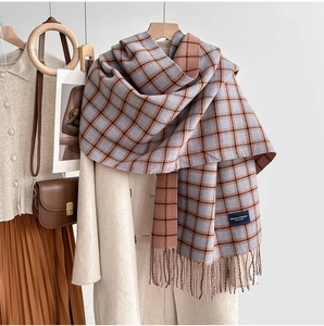 Detail of blue and orange plaid scarf with fringe paired with a cream wool coat