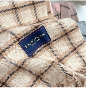 Macro detail of beige and brown plaid scarf featuring soft texture and fringe edges