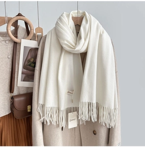 Detail shot of a soft cream cashmere-feel scarf with fringe edges and brand label