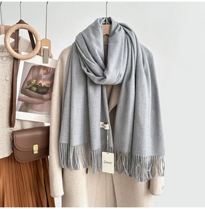 Detail of soft grey cashmere feel scarf with fine tassel edge and brand tag on beige coat