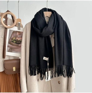 Detail of soft black cashmere-feel scarf featuring fine fringe and minimalist woven label