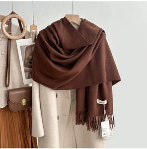 Close-up of soft dark brown fringe scarf texture with brand label on a beige coat
