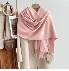 Close-up of pink tassel scarf detail with brand label on elegant beige winter coat