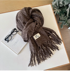 Detailed texture of coffee brown knit scarf with fringe and brand label on white table