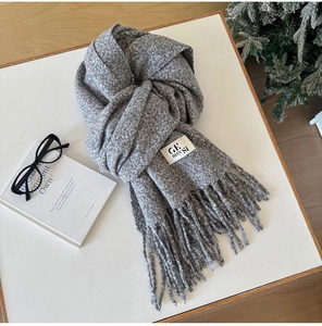 Close-up of thick grey knit scarf with tassels and fabric brand label detail