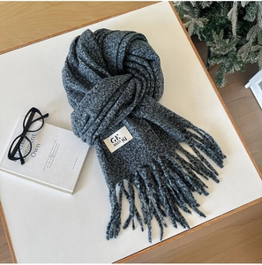 Close-up of thick knitted grey scarf texture with tassel edges and sewn-in woven label