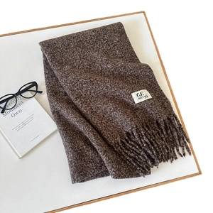 Thick dark brown tweed wool scarf with fringe and brand label on a white tray