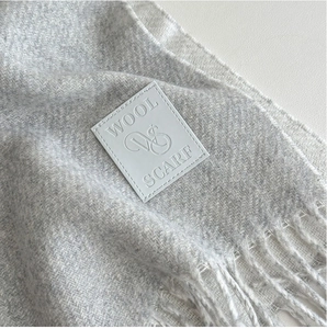 Primer plano de bufanda de lana gris con diseño de espiga y etiqueta blanca tejida
