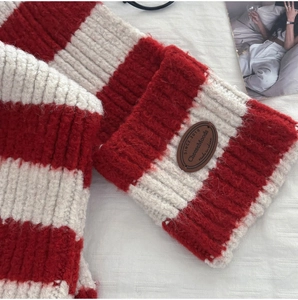 Detail of red and white striped knit scarf featuring a brown leather brand tag