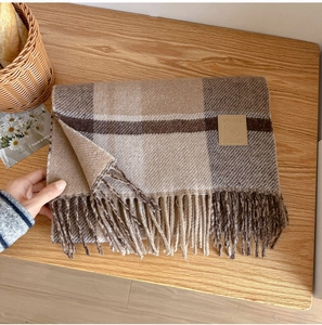 Detail of wool blend plaid scarf with leather label and fringe on wood background