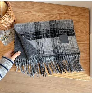 Close-up of wool plaid scarf with fringes and a leather label on a wooden background