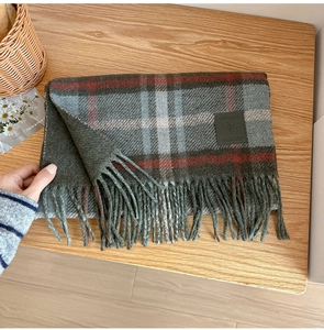 Macro detail of the wool blend plaid scarf with leather tag and decorative fringe