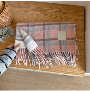 Detail of pink and grey plaid wool scarf with leather brand label and soft fringe texture