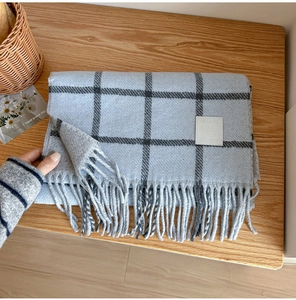 Macro view of blue and grey wool scarf with plaid pattern, fringe, and logo patch