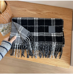 Close-up of wool plaid scarf with fringe edges and leather label on wooden background