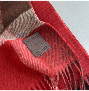 Macro detail of red and brown plaid wool scarf with leather logo tag and fringe