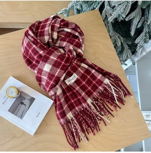 Detail view of a soft red and white checkered scarf with long tassels and a woven brand tag