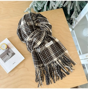 Close-up of thick plaid scarf with tassels and brand label on a wooden surface