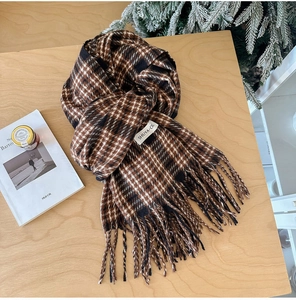 Detail of soft houndstooth scarf with fringe tassels and white label on wooden surface