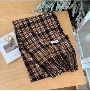 Detail of soft plaid scarf with tassels and white label on a wooden table setup