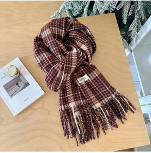 Close-up of classic plaid scarf with tassels and white brand label on wooden surface