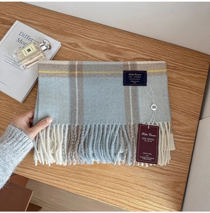 Detail of wool blend plaid scarf with tassels, featuring soft blue and beige knit texture