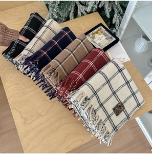 Detail view of multi-color plaid scarves with tassels on a cozy wooden background