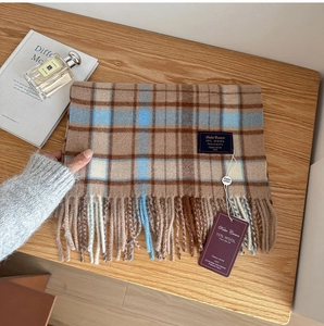 Detail of wool blend plaid scarf featuring camel and blue check with tassels on wood surface