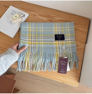 Detail of wool blend plaid scarf in blue and yellow with fringes on wooden surface