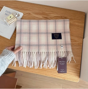 Detail of pink and grey check wool scarf with fringe edge and brand tags on wooden table