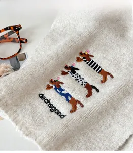 Detail of oatmeal knit scarf with three embroidered dachshunds and logo lettering