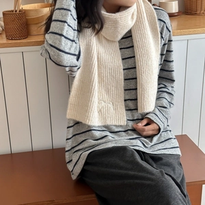 Close-up of cream knit scarf featuring delicate vertical ribs and bow embroidery detail