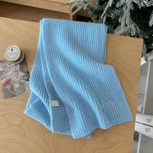 Detail of light blue knit scarf with bow embroidery and ribbed texture on wooden surface
