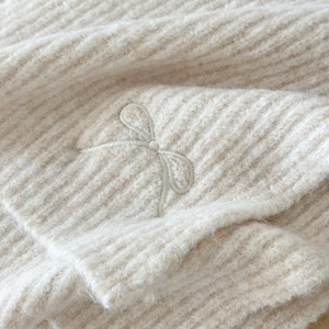 Macro detail of cream wool blend ribbed knit scarf with subtle bow embroidery