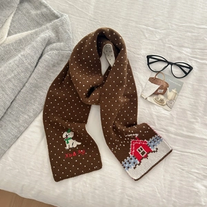 Detail of coffee knit scarf with white dots, dog embroidery, and snowy house pattern
