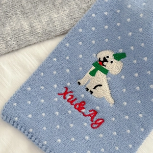 Detailed close-up of sky blue knitted scarf featuring white dots and cute dog embroidery