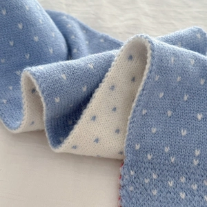 Detailed close-up of light blue and white knitted scarf featuring delicate heart patterns
