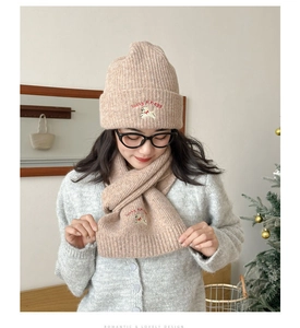 Detailed close-up of beige knitted hat and scarf set with cute dog embroidery details