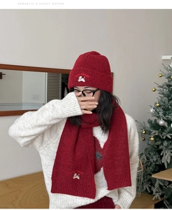 Model wearing red knitted hat and scarf set with running dog embroidery in Christmas setting.