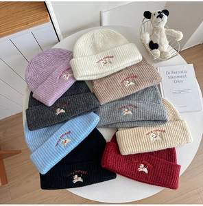 Close-up of nine assorted colors knitted beanies with puppy embroidery and red lettering