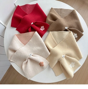 Detail of red and neutral knitted scarves with white flower motifs on a white surface