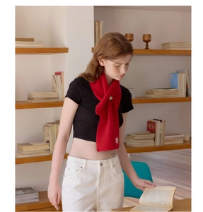 Detail of red knitted scarf with white floral embroidery and stylish cross-wrap design