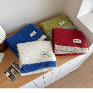 Close-up of stacked colorful chunky knit scarves with branded labels on a wooden rack