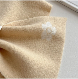 Close-up of a soft knitted scarf showing floral pattern and plush texture in beige color