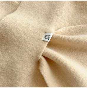 Close-up of beige knitted scarf featuring soft plush texture and minimalist logo label