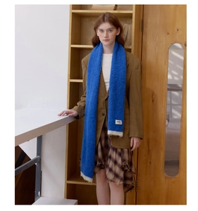 Detail of royal blue knit scarf featuring white fringe and stylish fabric brand tag
